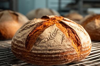 Round sourdough loaf with a scored wheat pattern cooling on a bakery rack