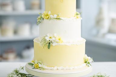 Pale lemon and elderflower tiered cake decorated with white icing and small edible flowers